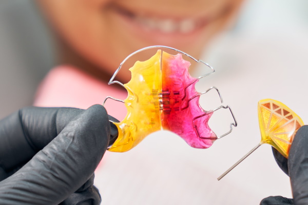 Close up of hands in black rubber medical gloves holding colorful braces. Dentist showing metal braces for african smiling girl. Concept correction and improving bite, health and beauty.